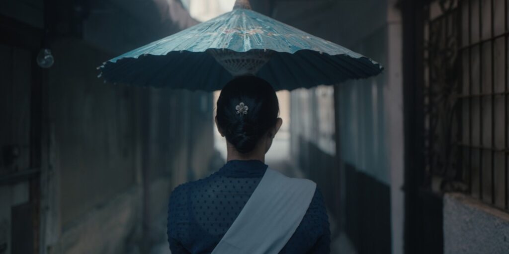 영화 나나 스틸컷 주인공 나나가 우산을 쓰고 좁은 골목길을 걸어가고 있다